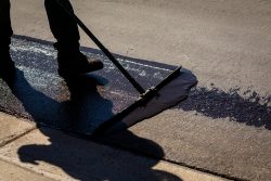 Worker,Using,A,Sealcoating,Brush,During,Asphalt,Resurfacing,Project